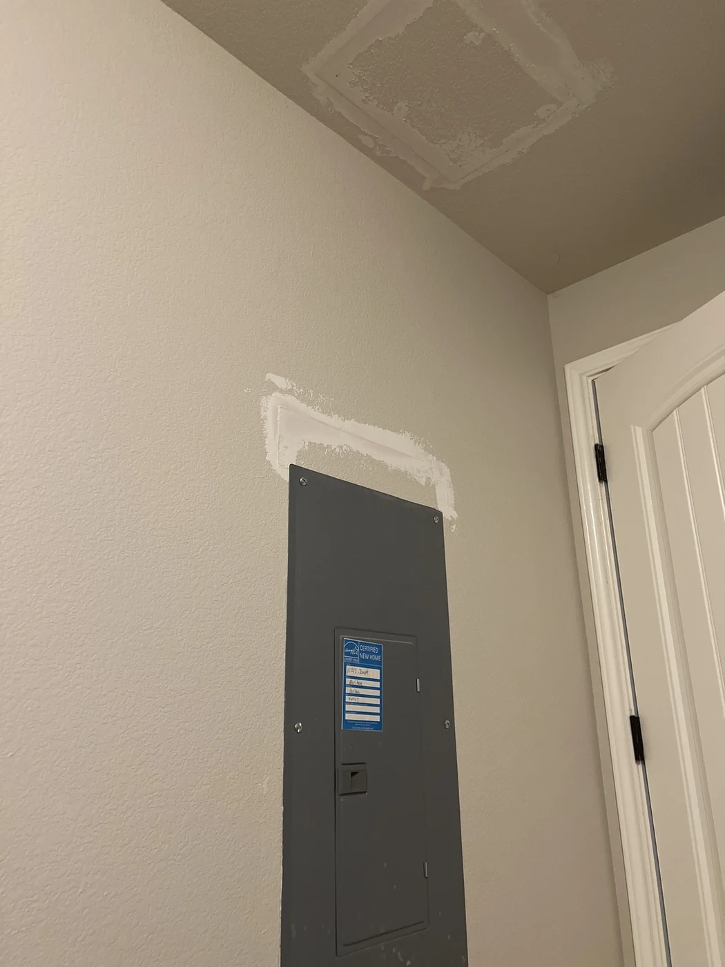 Wall-mounted electrical panel with patches in the surrounding wall and ceiling.