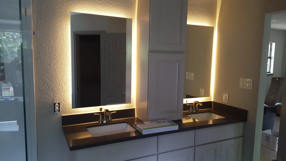 Two bathroom mirrors with warm perimeter lighting above a double vanity.