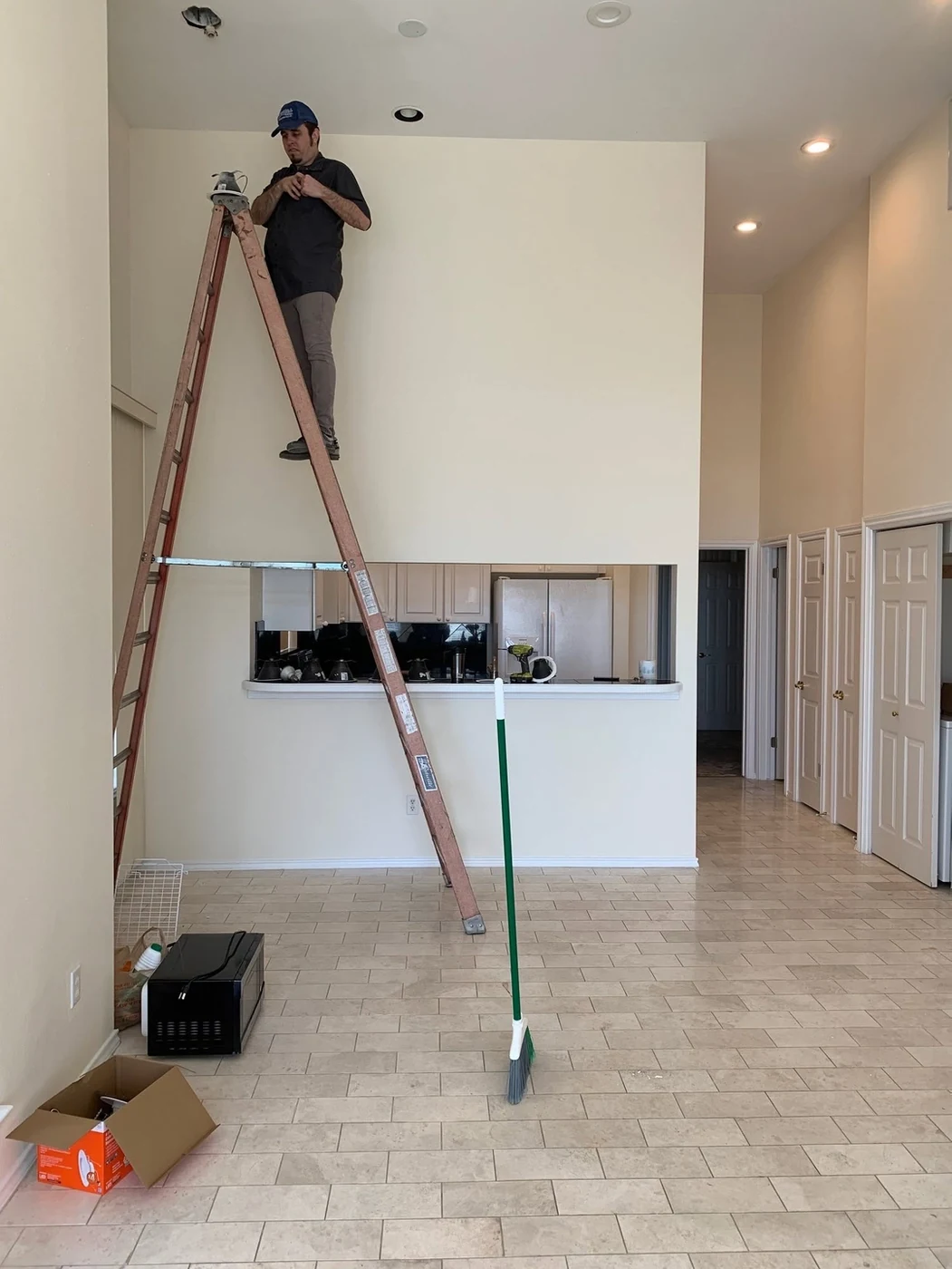 A worker on a ladder beneath ceiling light openings in a living room.