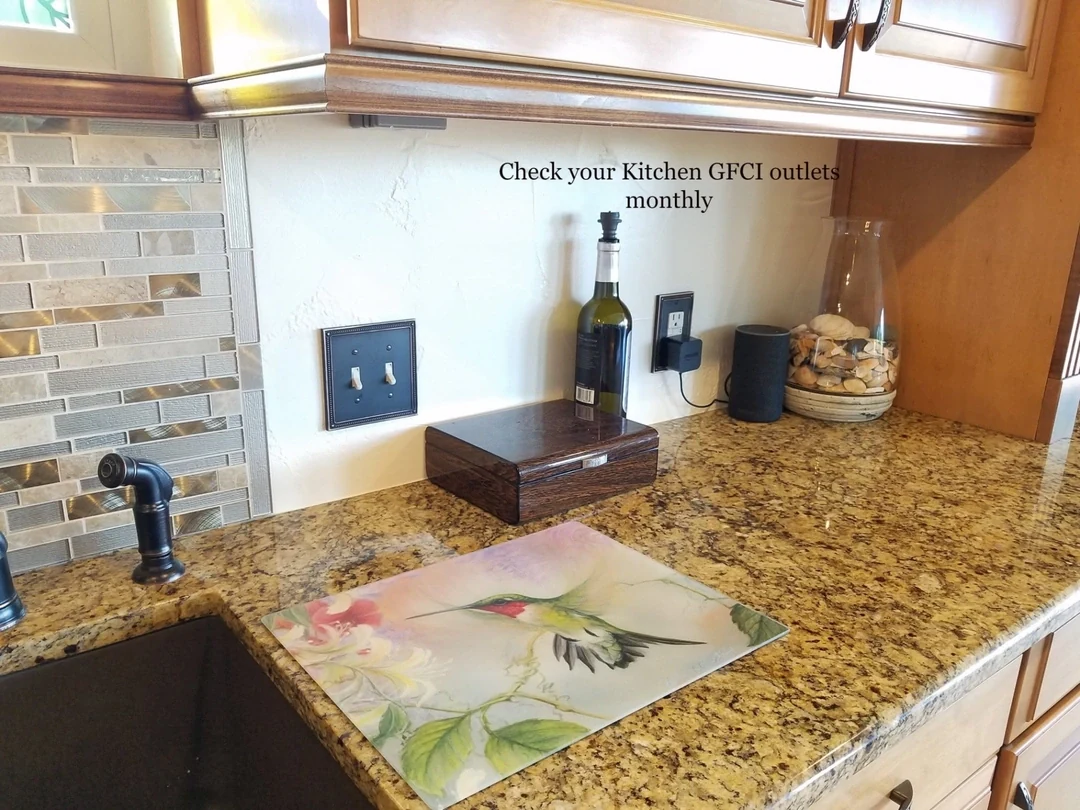 Kitchen countertop and electrical outlets below wood cabinets, with a reminder to check GFCI outlets monthly.
