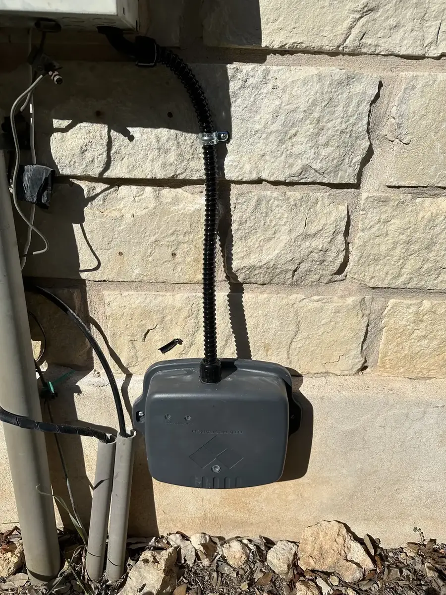 Covered electrical outlet and conduit mounted on a stone wall.
